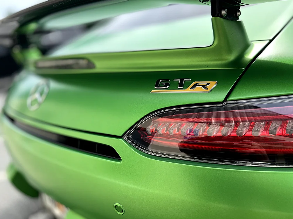 Close-up of the rear of a metallic green Mercedes-AMG GT R, highlighting the "GTR" badge, LED taillight, and the aggressive rear wing.