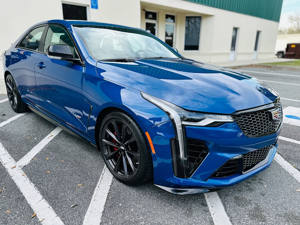 Blue Cadillac CT4-V parked in a lot, shown from a front-side angle, featuring black alloy wheels, vertical LED headlights, and a sporty front grille.