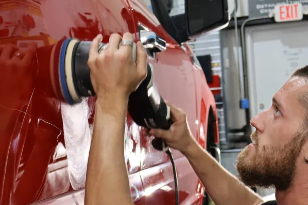 A focused man uses a dual-action polisher on the side of a red vehicle during the paint correction stage, an essential prep step in the ceramic coating process. This image visually supports the comparison of DIY vs Professional Ceramic coating by highlighting the skill and tools involved in professional application.